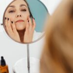 Mulher aplicando hidratante facial no rosto em frente ao espelho