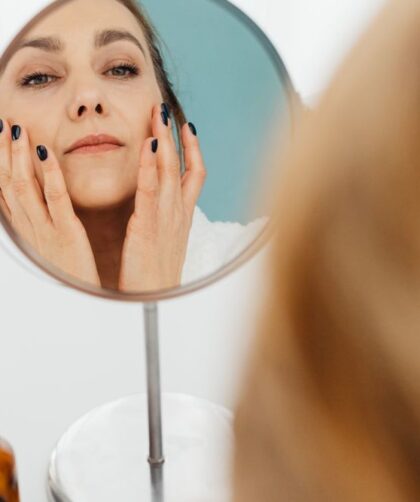 Mulher aplicando hidratante facial no rosto em frente ao espelho