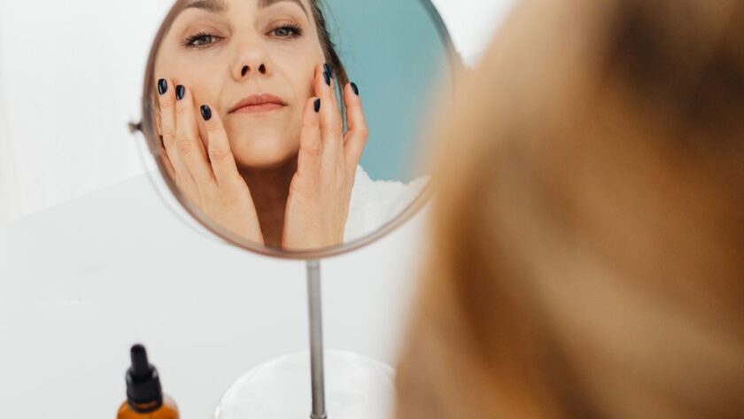 Mulher aplicando hidratante facial no rosto em frente ao espelho