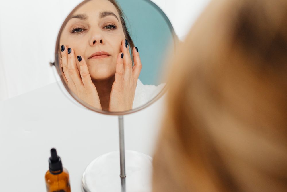 Mulher aplicando hidratante facial no rosto em frente ao espelho